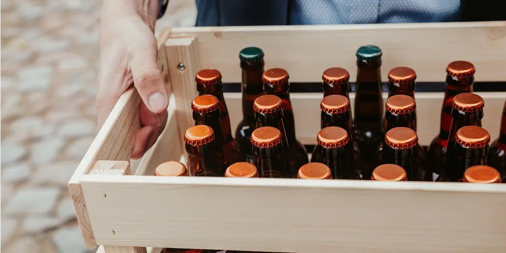 Man,Carrying,Wooden,Crate,Full,Of,Unmarked,Beverage,Bottles.